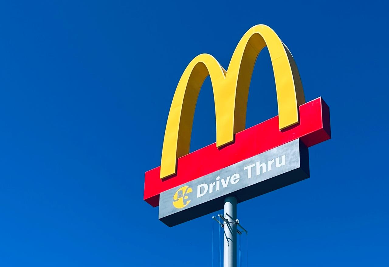 Totem publicitário do McDonald's com o icônico logotipo dos arcos dourados e uma placa com a inscrição "Drive Thru"